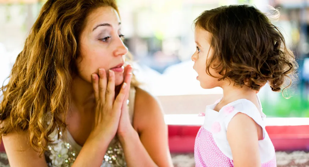 A child plays quietly with wooden blocks while a parent talks in the background.
