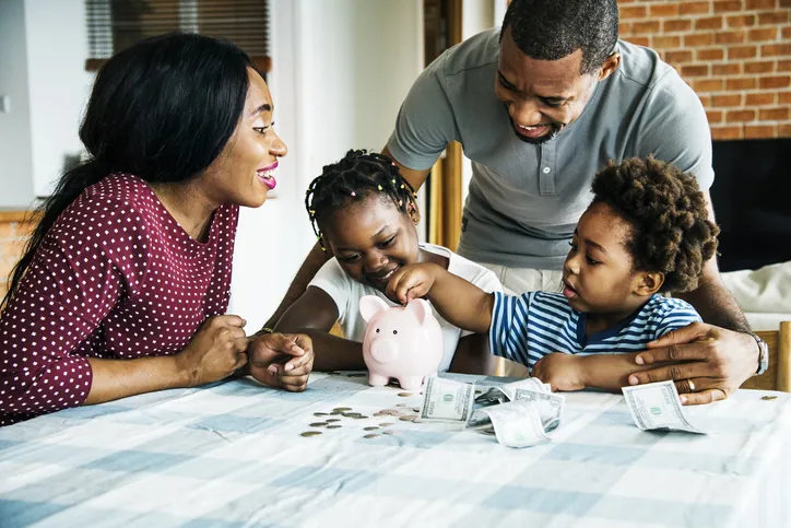 A parent teaching a young child basic financial literacy using a clear piggy bank.