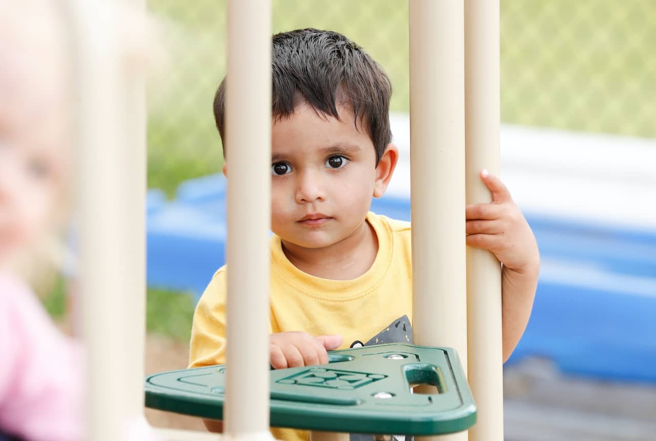 A calm caregiver interacts patiently with an overwhelmed toddler in a classroom.